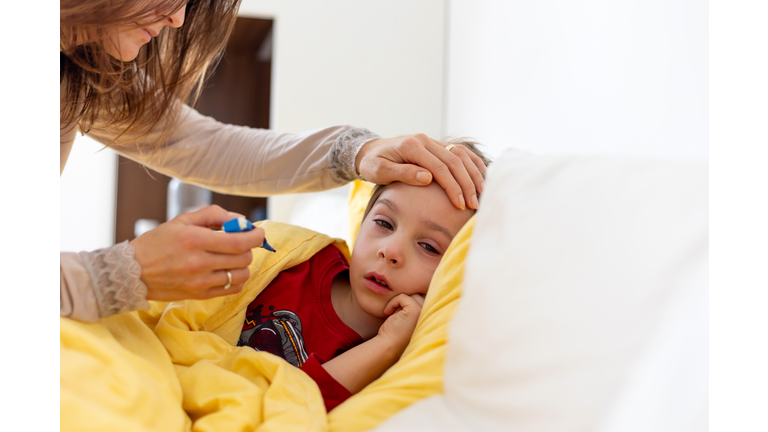 Sick child, toddler boy lying in bed with a fever, having breakfast, resting at home