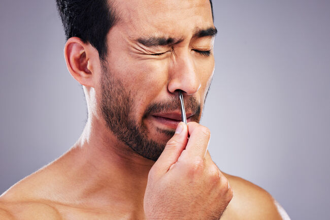 Plucking hair, nose and a man with tweezers for grooming, hygiene and beauty on a studio background. Pain, face and an Asian person with tools for cosmetics or facial care isolated on a backdrop