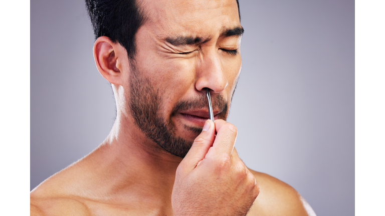 Plucking hair, nose and a man with tweezers for grooming, hygiene and beauty on a studio background. Pain, face and an Asian person with tools for cosmetics or facial care isolated on a backdrop