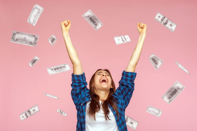 Money rain, woman rising hands up with toothy smile on face, pleased, amazed with money falling.
