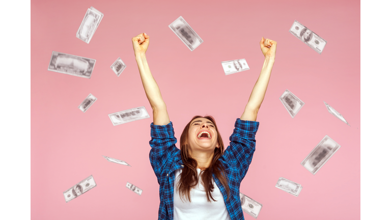 Money rain, woman rising hands up with toothy smile on face, pleased, amazed with money falling.