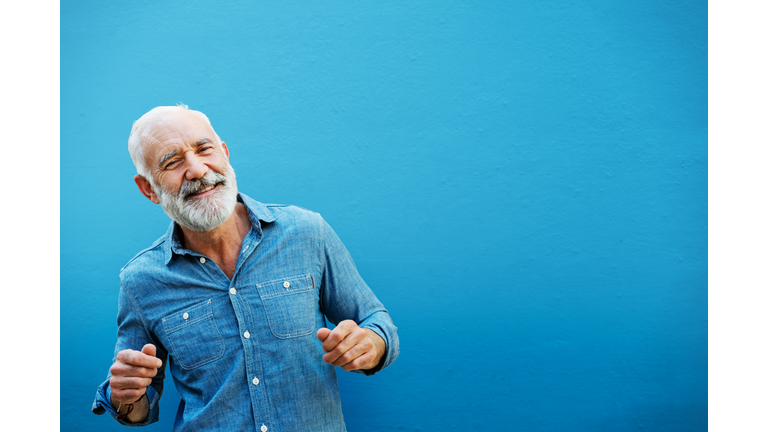 Happy man dancing next to blue wall, outside