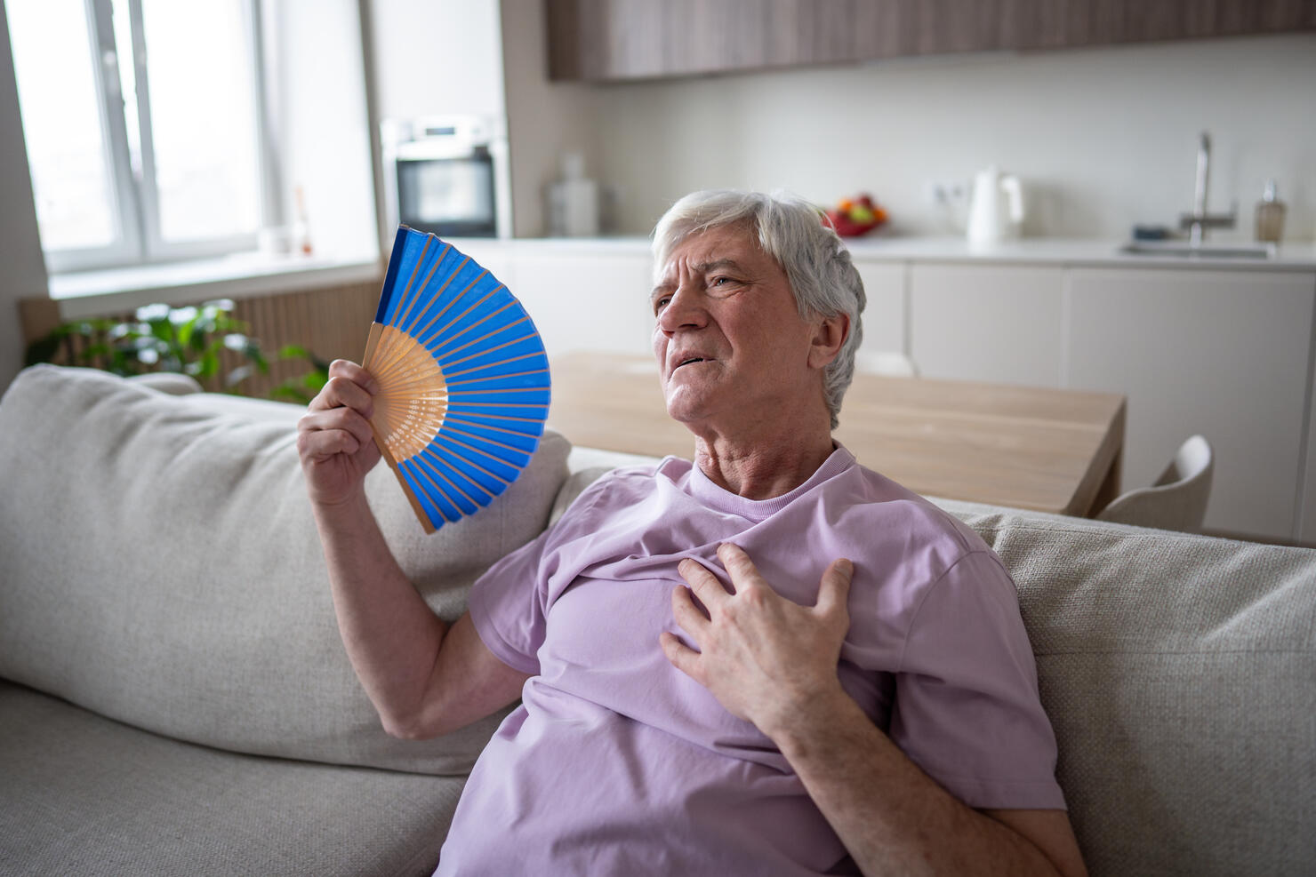 Sweating elderly man fanning suffering from suffocating heat nausea and heart attack at home