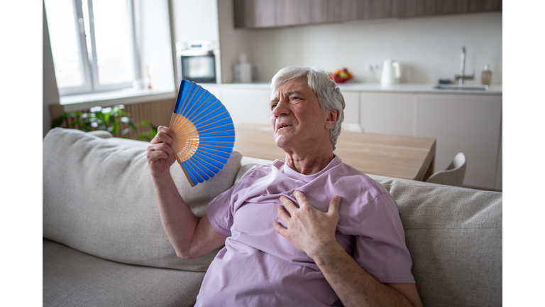 Sweating elderly man fanning suffering from suffocating heat nausea and heart attack at home
