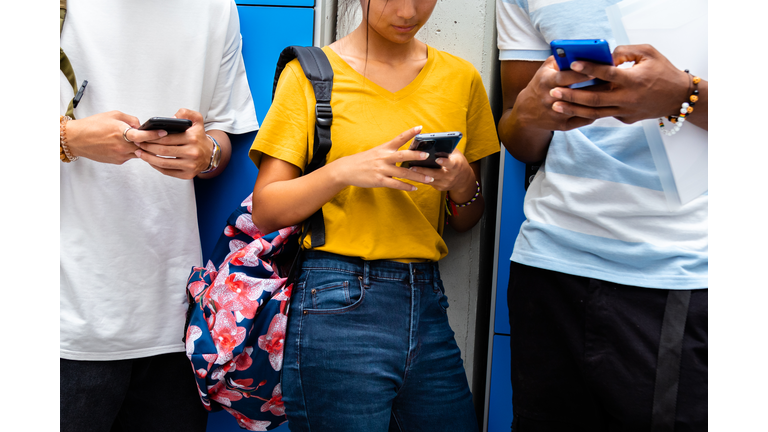 Close-up of teen high school students using mobile phone in school corridor.