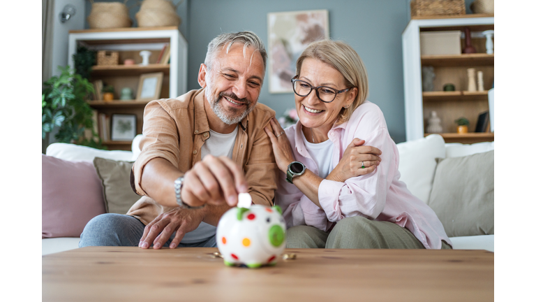 Mature couple inserting coins in a piggybank