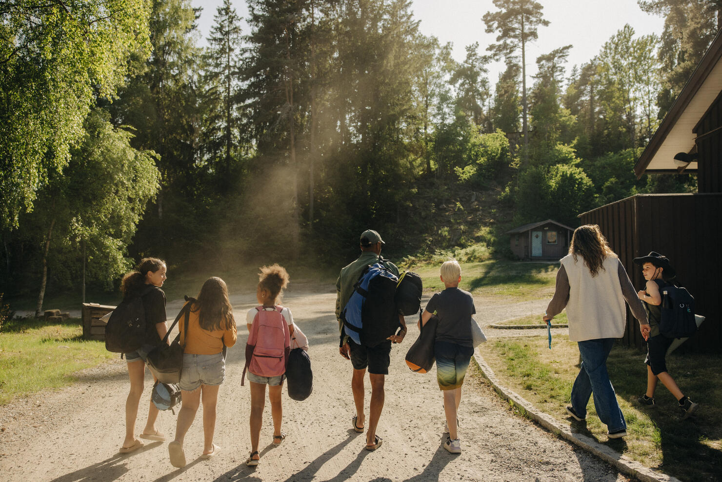 Rear view of kids walking on footpath with counselors at summer camp