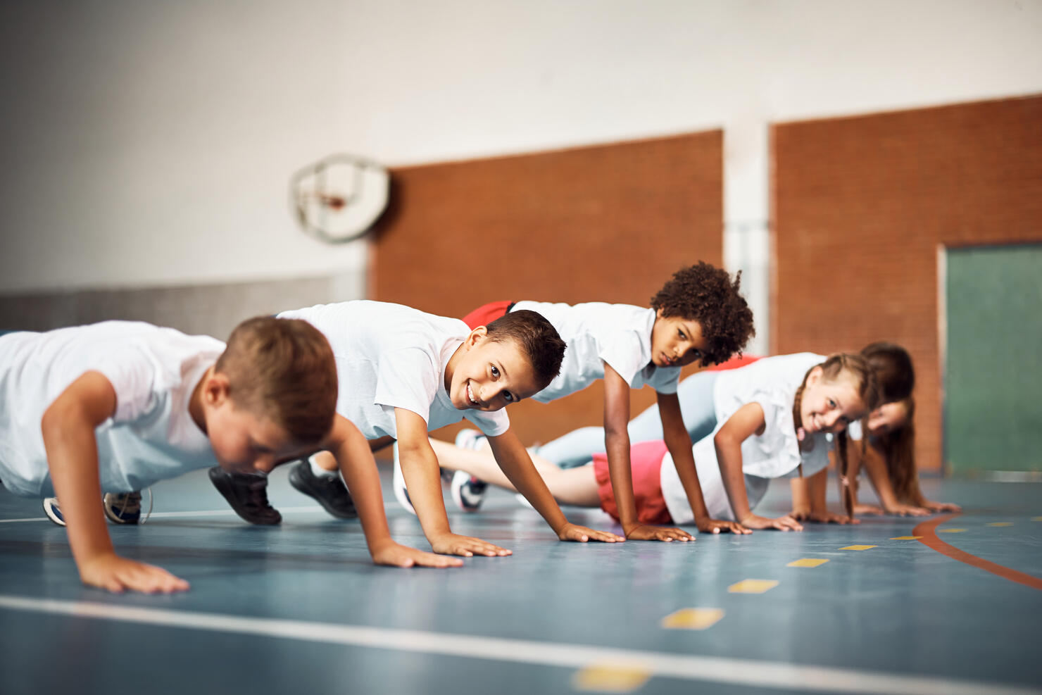 Happy school kids exercising push-ups on physical education class at school gym