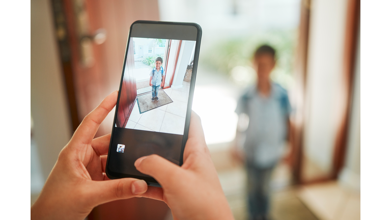 Closeup of mother taking photo of son on first day of school.   Hands taking picture on cellphone of kindergarten boy standing by the door and ready to leave home. Proud mom documenting childhood