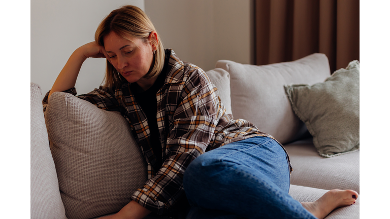 Upset woman sitting in living room on sofa. Concept of stress, depression, illness.