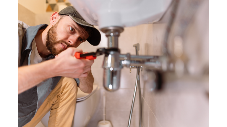 A plumber carefully fixes a leak in a sink using a wrench