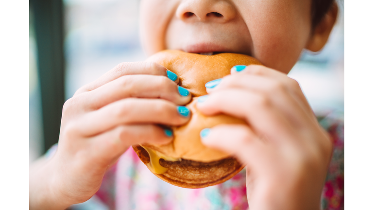 Close-up of child enjoying a cheeseburger with brightly painted nails