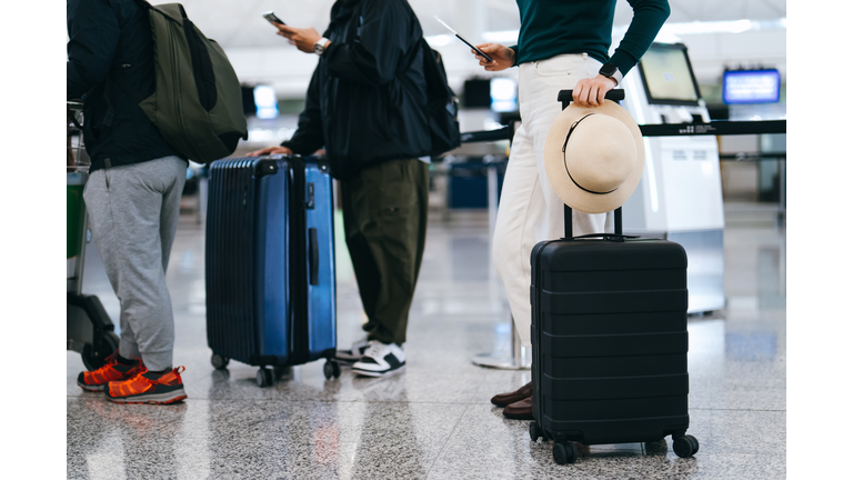 Cropped shot of group of airline passengers with suitcases standing in queue, waiting at check-in counter at International airport. Ready for a trip. Business travel. Travel and vacation concept