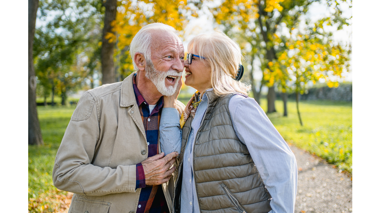 Senior woman whispering to husband's ear outdoors