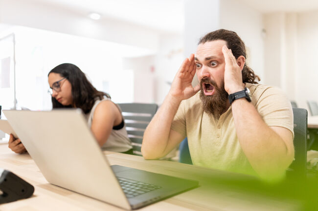 Businessman working on laptop feeling surprised about news