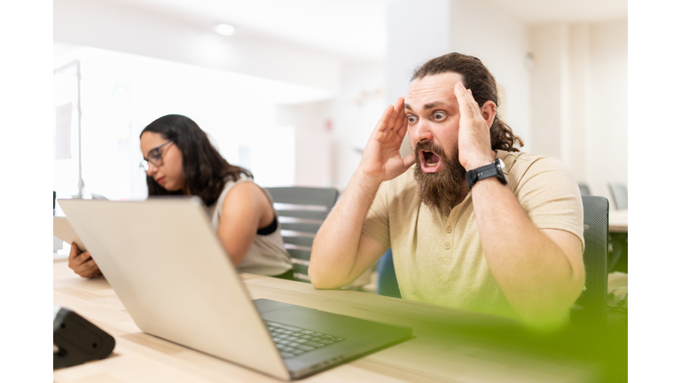 Businessman working on laptop feeling surprised about news