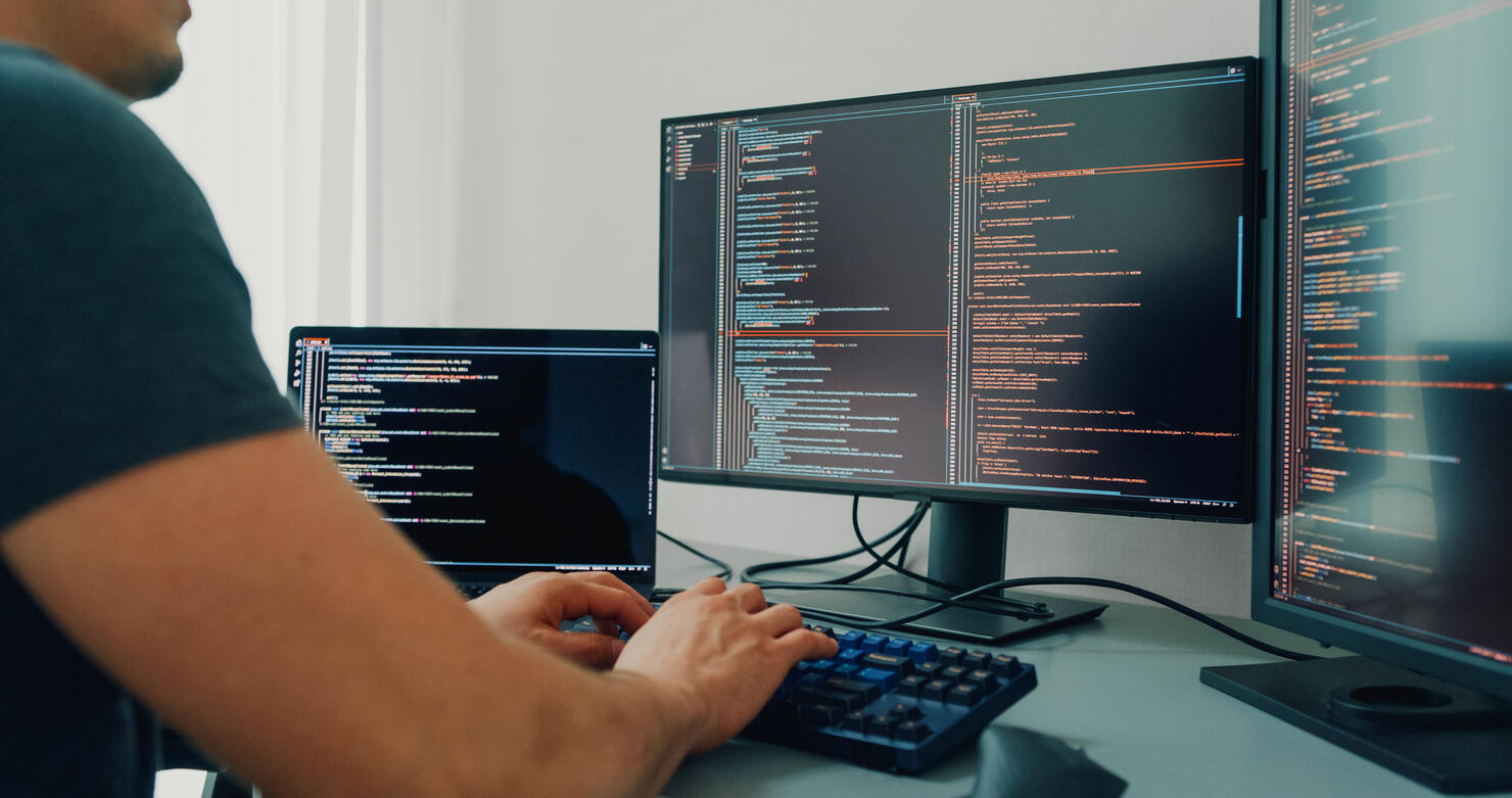 Closeup young man software developers using computer to write code application program for AI technology development at desk with multiple screens work at home office. Programmer development.