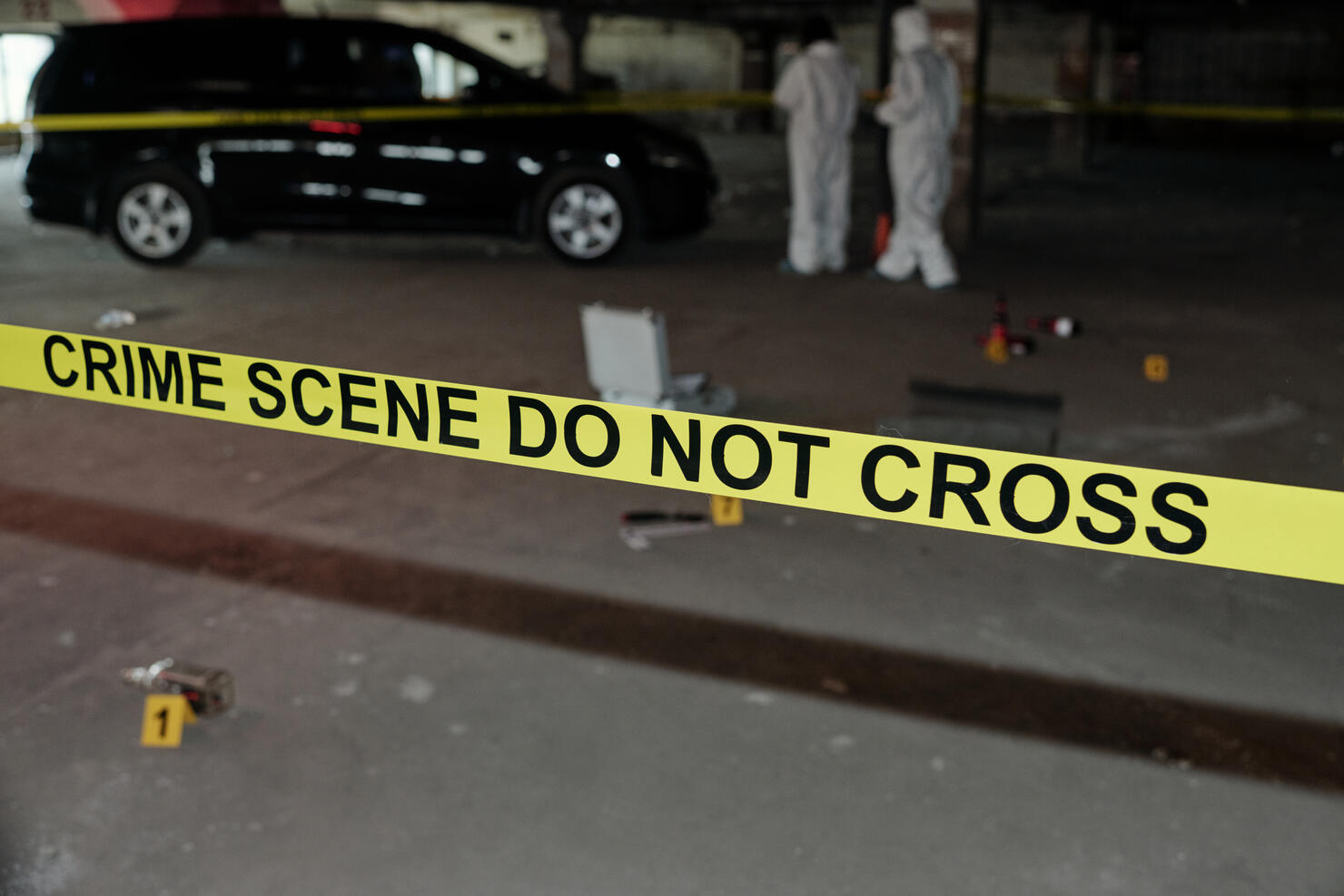 Yellow tape surrounding crime scene in parking area with two experts