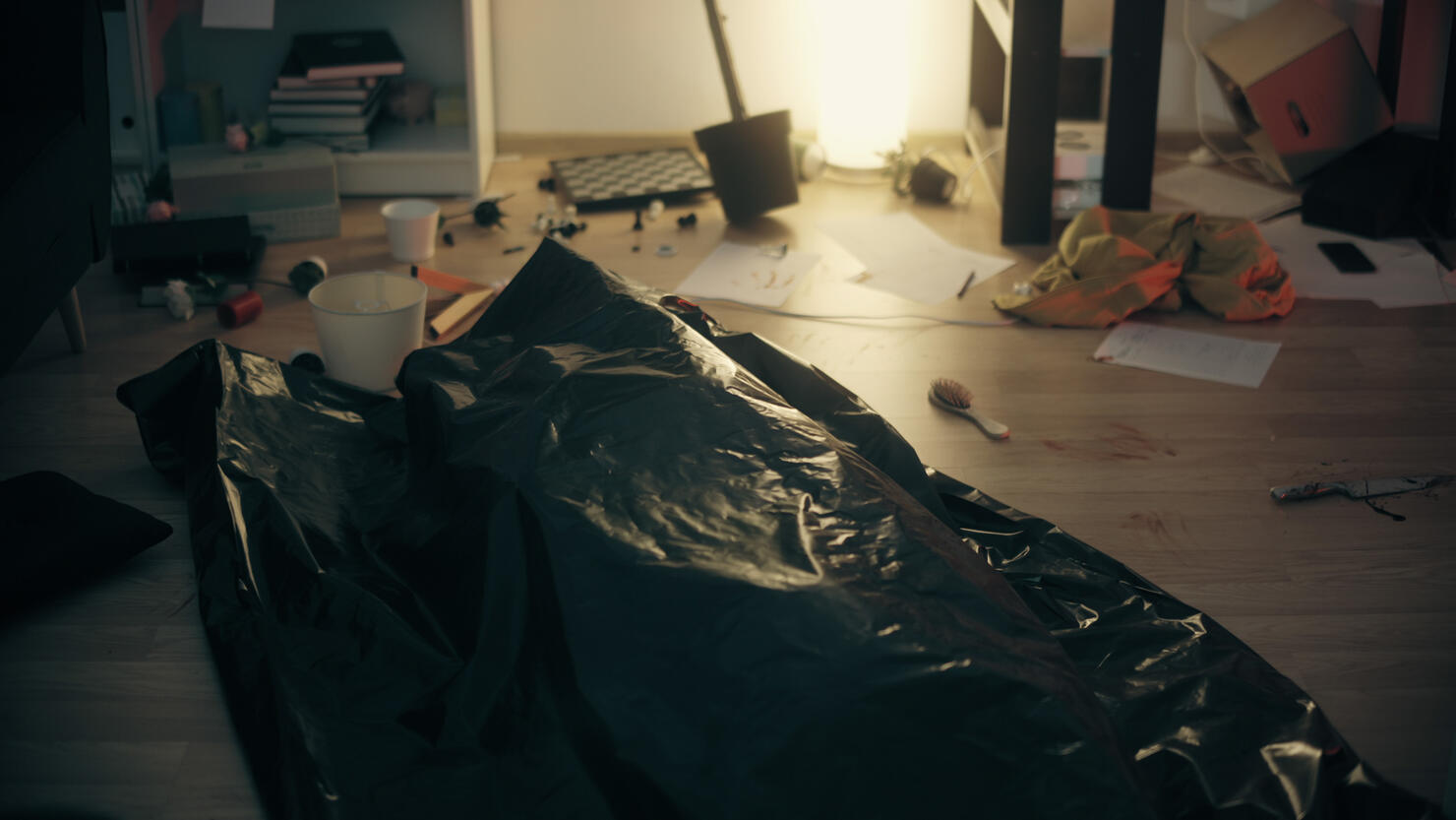 A dead body lies in a bag in a trashed apartment, showing signs of struggle - a murder victim