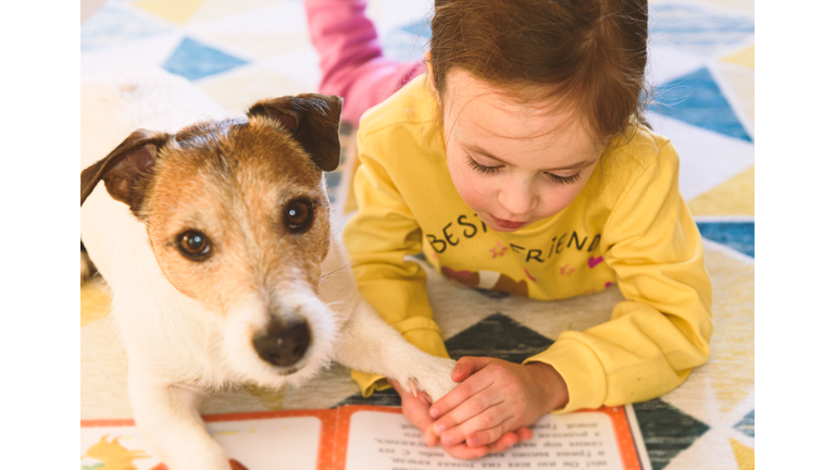 Small girl learning to read. Kid is reading a book to her pet dog.