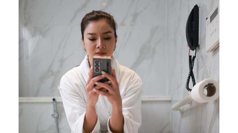 Asia Woman using mobile phone on toilet bowl in restroom, Home living lifestyle ,Daily routine. Lifestyle and technology