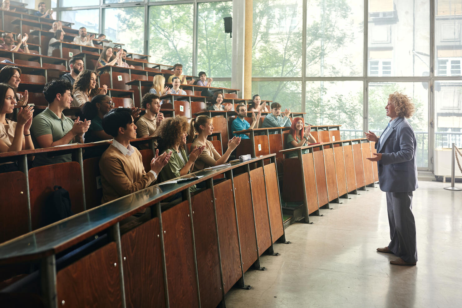 Crowd of happy students applauding to their professor in amphitheater.