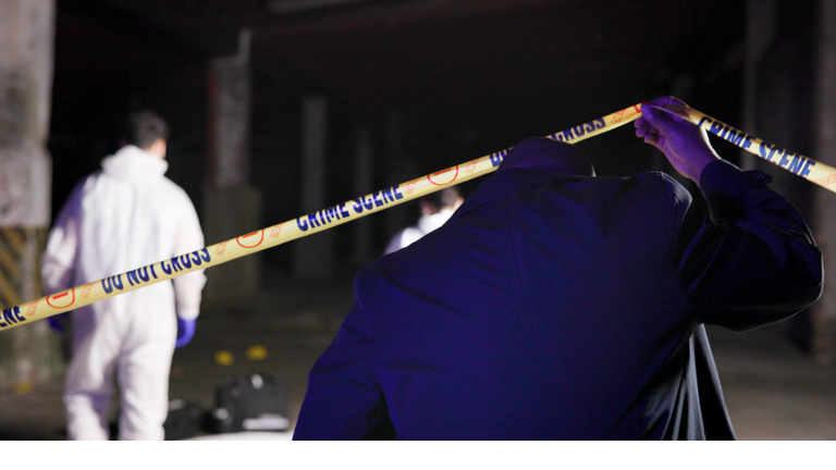 Detective, yellow tape and back at crime scene with forensic team, inspection and outdoor at night. Police, csi and barrier for investigation, evidence and search for lead, emergency and law in city