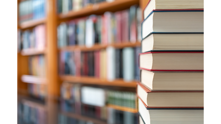 Many books stacked with blurred background of bookstore full of books. Photo with copyspace.