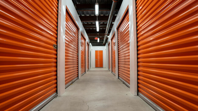 Empty hallway with orange  garage doors of a self storage unit warehouse.