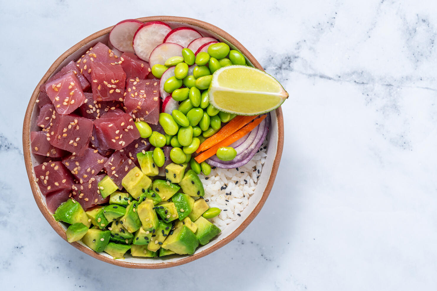 Tuna Poke bowl on white marble with Edamame, avocado and radish.