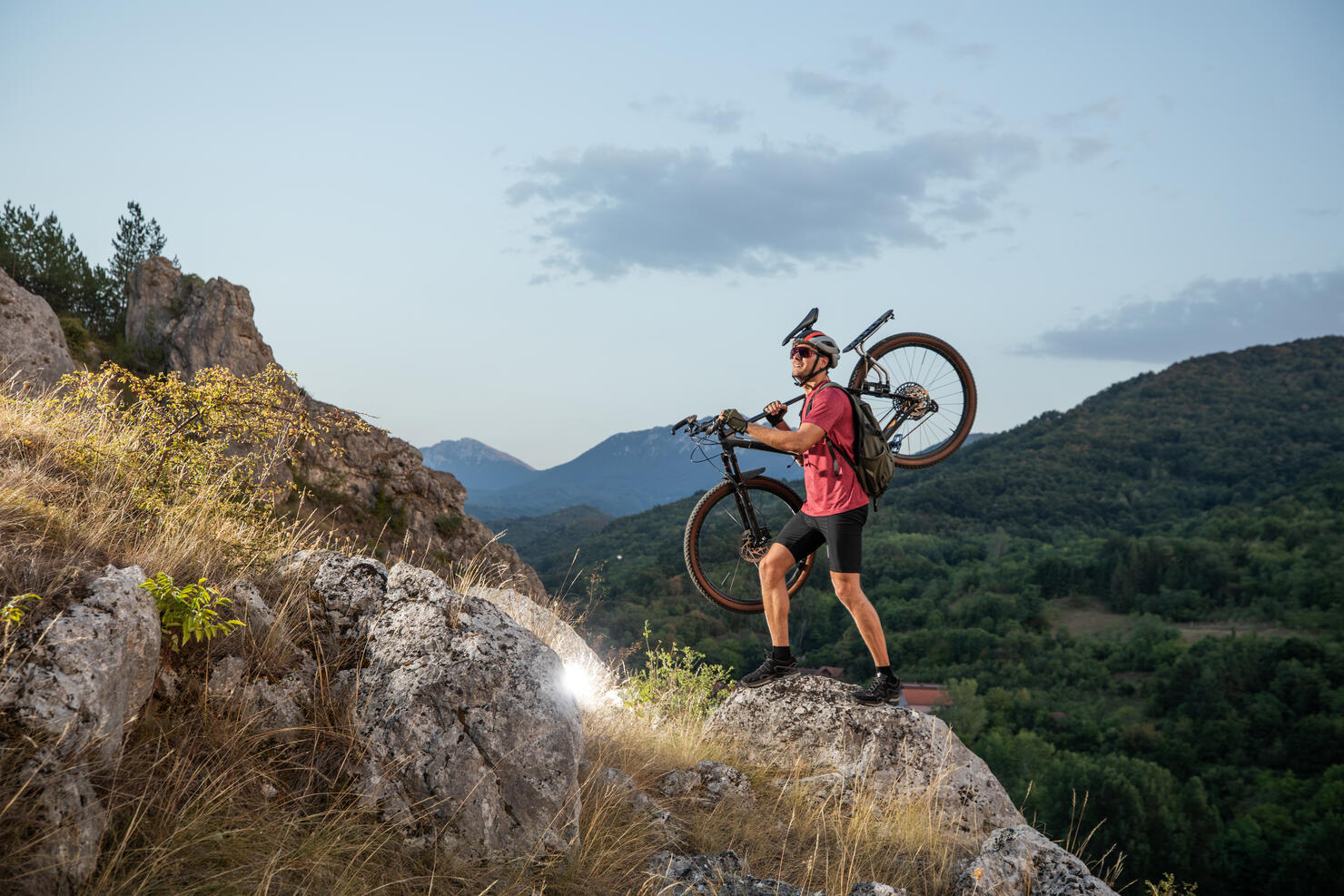 Cyclist Carrying Mountain Bike on Rocky Path in Wilderness at Sunrise