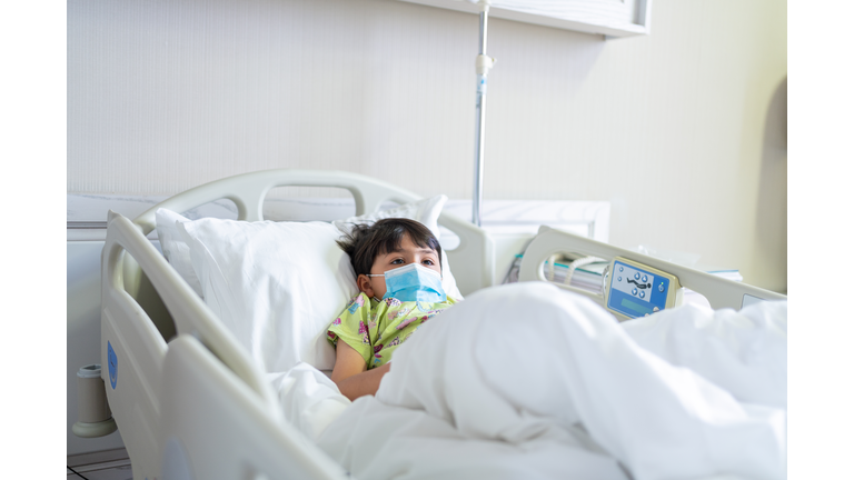 Little child patient with protective face mask lying on bed at hospital