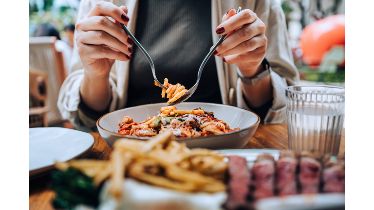 Close-up, mid-section of young Asian woman sitting at dining table holding cutleries, twirling freshly served spaghetti bolognese and enjoying her meal in restaurant. Dining out. People, food and lifestyle