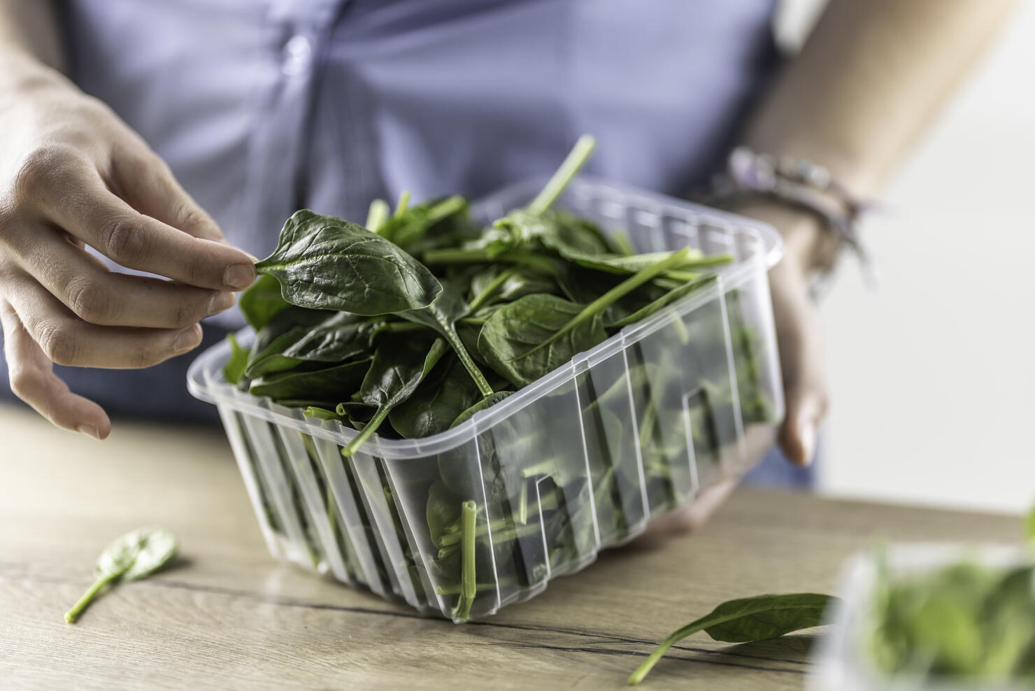 Female hands hold a plastic package with baby spinach in her kitchen.