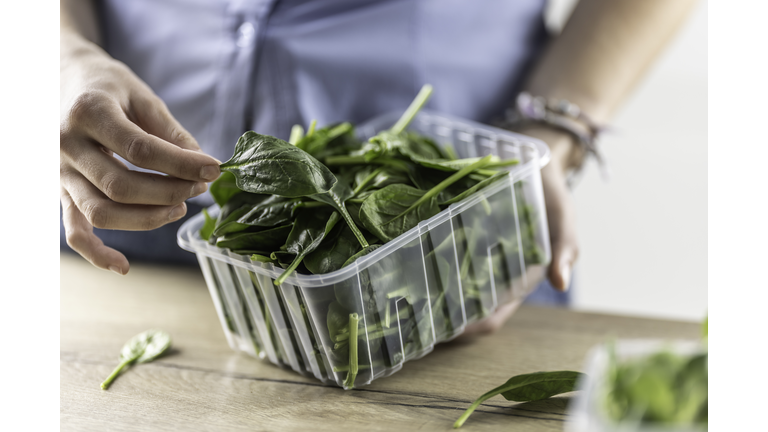 Female hands hold a plastic package with baby spinach in her kitchen.