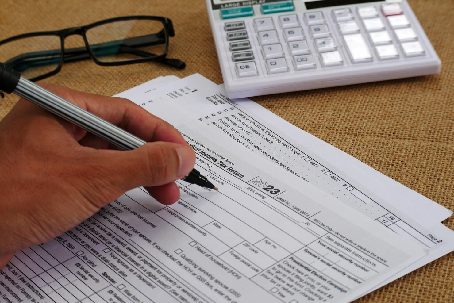 Businessman's hand is writing on a tax form, there is a calculator and glasses on the table
