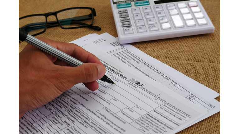 Businessman's hand is writing on a tax form, there is a calculator and glasses on the table
