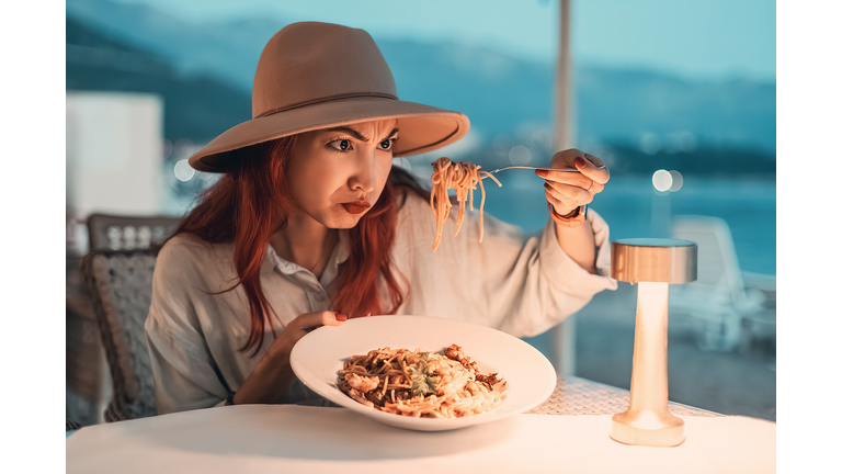 Woman disgusted by her spaghetti while dining in restaurant by the sea