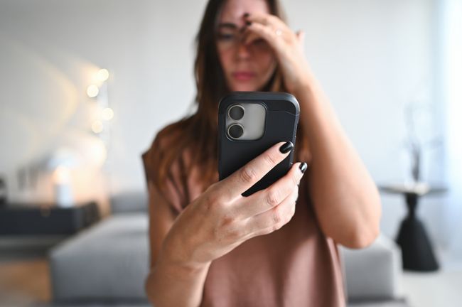 Woman feeling stressed, having headache from phone overuse