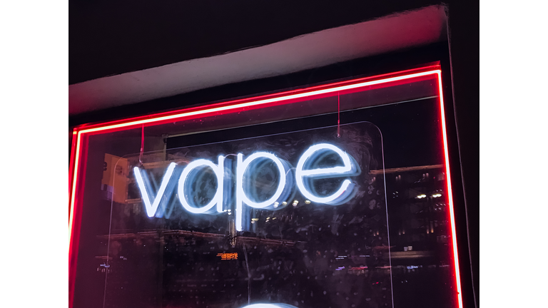 vape shop electronic cigarette neon colored window showcase sign lights up attracting customers on the street at night.