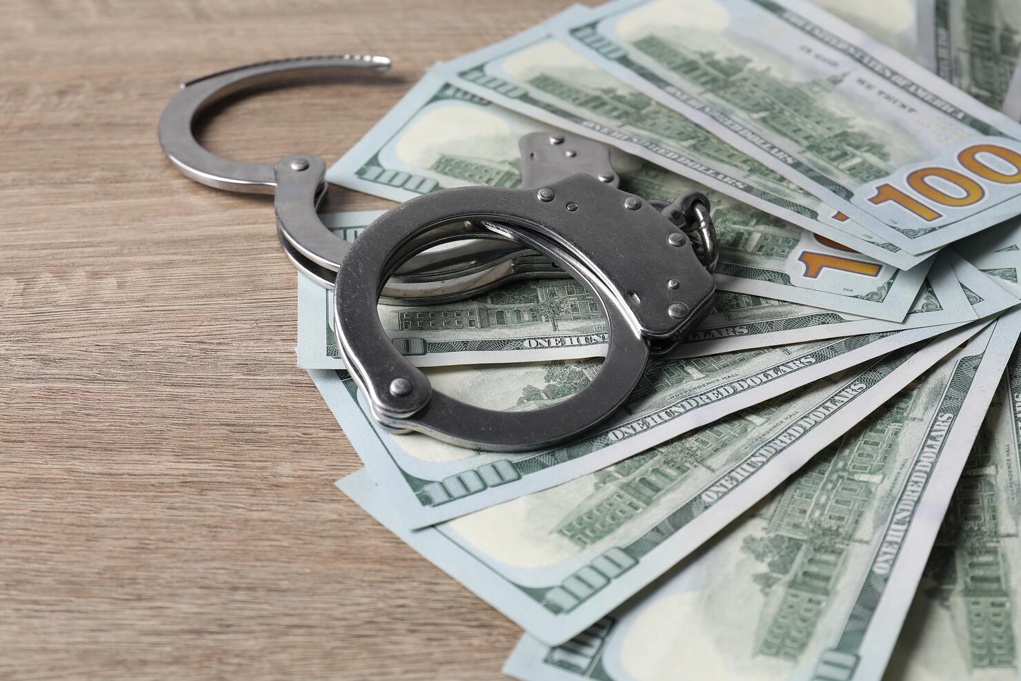 Corruption. Handcuffs and dollar banknotes on wooden table, closeup