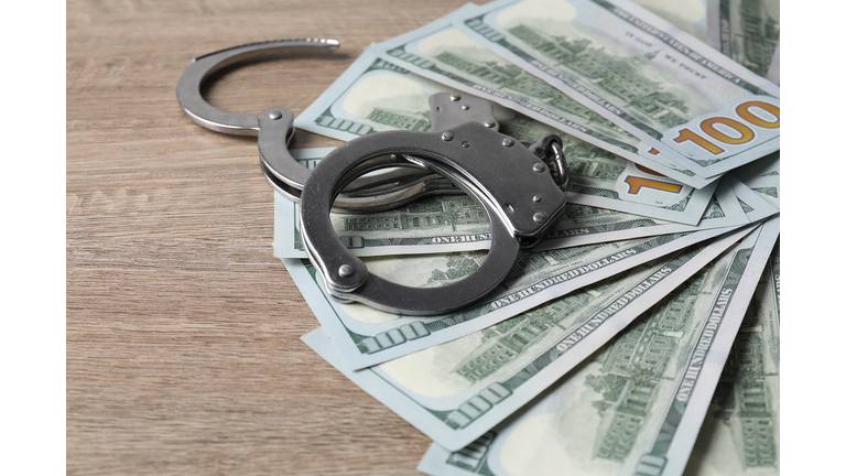 Corruption. Handcuffs and dollar banknotes on wooden table, closeup
