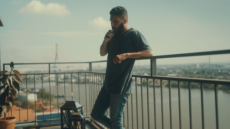 Man smoking in front of balcony to relieve stress from work.