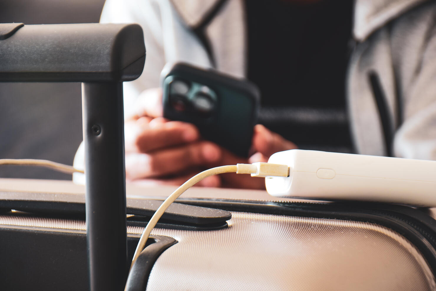 Cropped image of a South Asian man waiting in airport lounge charging his phone using power bank before departure. Focus on the foreground.