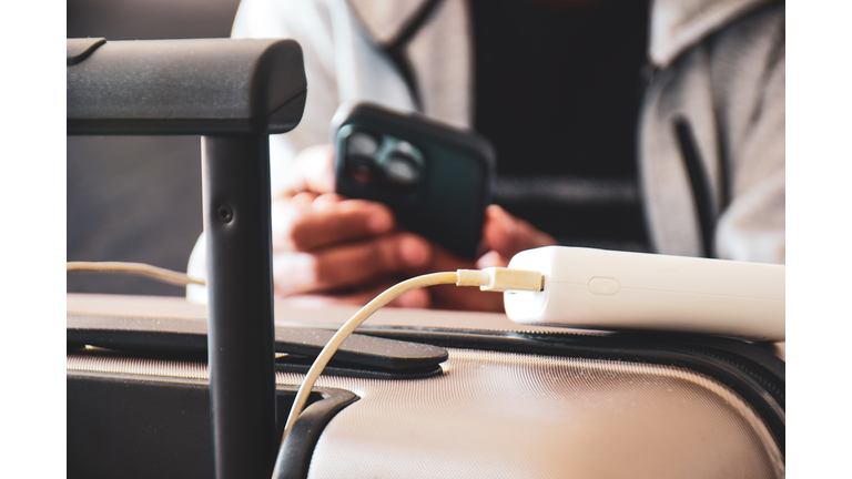 Cropped image of a South Asian man waiting in airport lounge charging his phone using power bank before departure. Focus on the foreground.