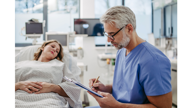 Doctor talking with worried patient before surgery, writing medical document. Emotional support before surgery. Friendly male doctor reassuring patient.