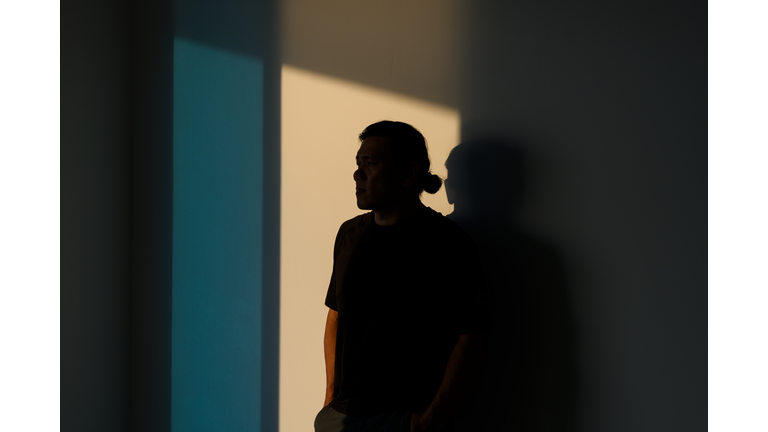 A man, completely obscured in shadow looks away