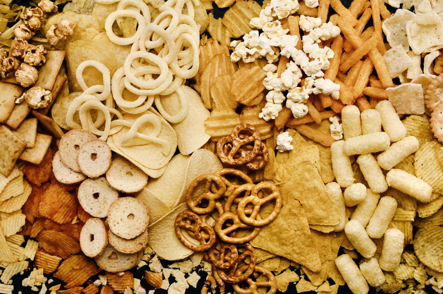 Colorful mix of salty snacks for beer varieties: chips and pretzels, onion rings and crackers.