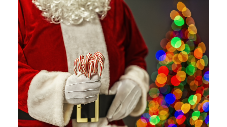 Santa Claus with a fist full of candy canes and bokeh from Christmas tree in the background
