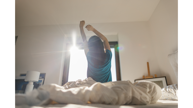 Young woman waking up and stretching after waking up in her bedroom